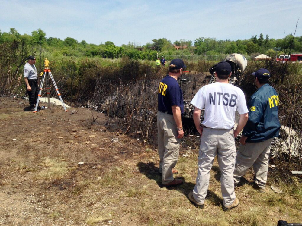 This photo provided by the National Transportation Safety Board, shows NTSB investigators at the scene of a plane that plunged down an embankment and erupted in flames during a takeoff attempt Saturday night at Hanscom Field in Bedford, Mass.