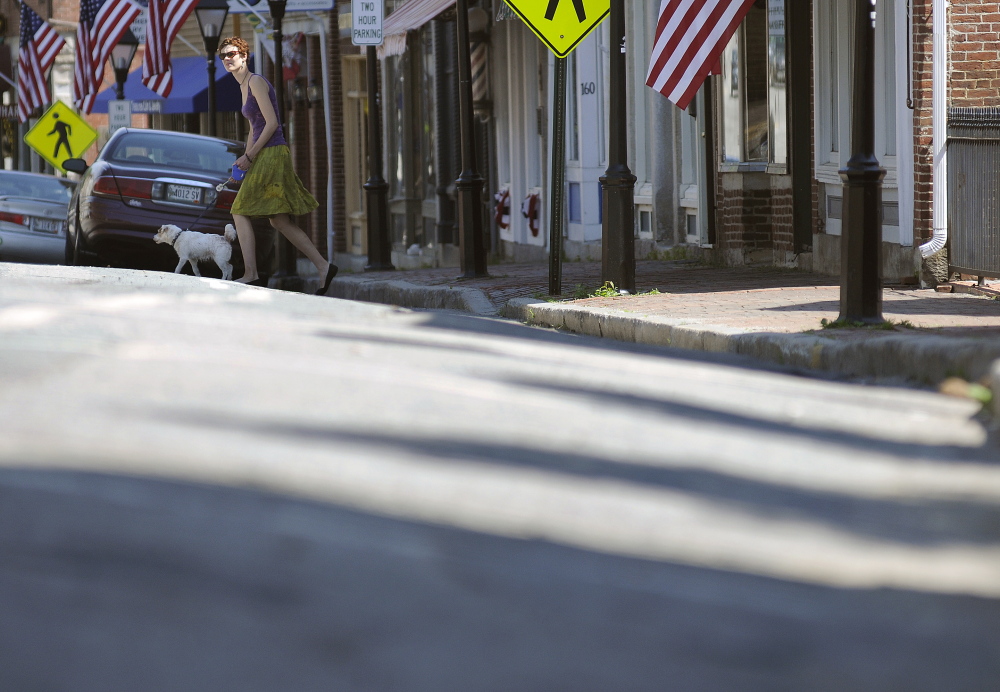 Staff photo by Andy Molloy A NEEDED FIX: A woman walks her dog Monday across Water Street in Hallowell, which has an elevated crown in the middle.