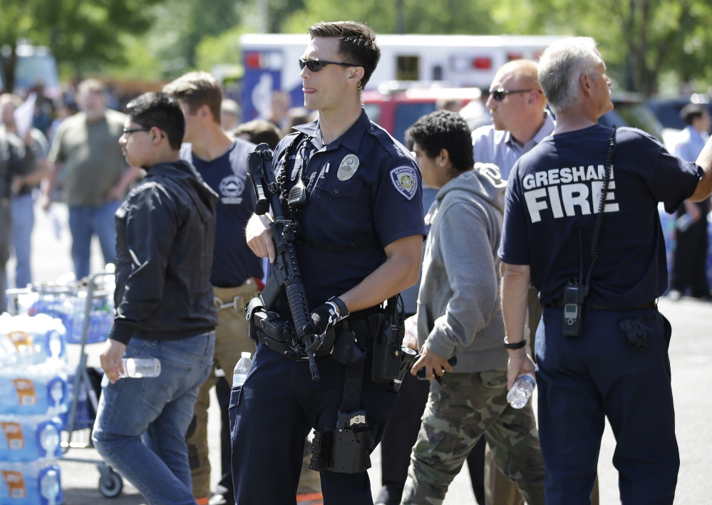 A police officer stands guard as students arrived by bus at a shopping center parking lot in Wood Village, Ore., after a shooting at Reynolds High School Tuesday, June 10, 2014, in nearby Troutdale. A gunman killed a student at the high school east of Portland Tuesday and the shooter is also dead, police said. (AP Photo/Rick Bowmer)