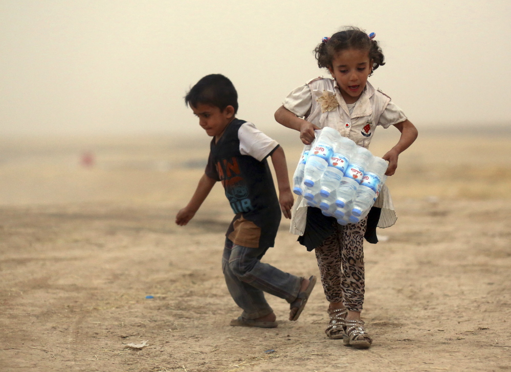 A girl who fled the violence in the Iraqi city of Mosul carries a case of water at a camp on the outskirts of Arbil in Iraq’s Kurdistan region.