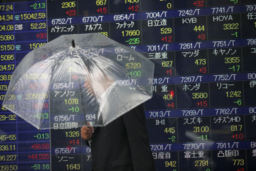 In this file photo, a man holding an umbrella walks past an electronic stock indicator of a securities firm, in Tokyo. The Treasury Department releases foreign holdings data for April on Monday.