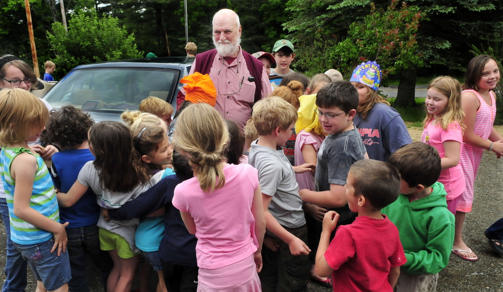 APPRECIATION: William Crumley is surrounded by hugging students at the Cornville Regional Charter School during a ceremony marking his leaving as school principal on Wednesday. An American flag was raised and lowered and presented to Crumley and a time capsule was sealed during the event.