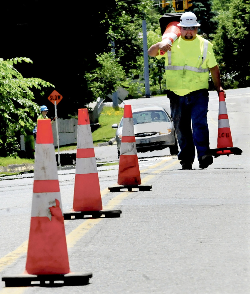 Mark Franzose picks up some of the dozens of traffic cones that were used by workers installing a natural gas pipeline on Cool Street in Waterville on Monday.