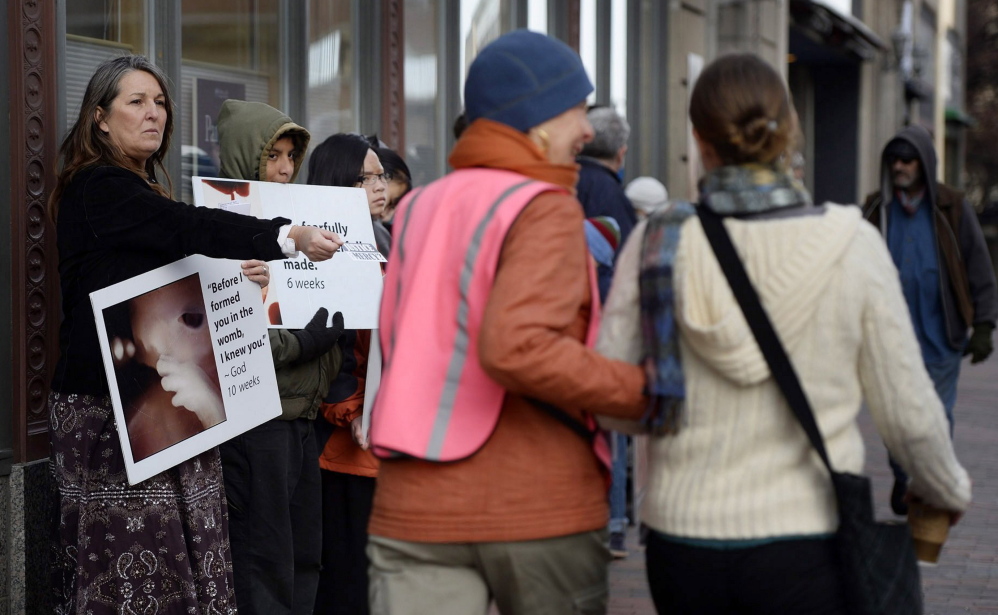 As Leslie Sneddon of Richmond offers literature near Planned Parenthood in Portland, a volunteer escorts a woman past protesters on Nov. 15, 2013. Three days later, the City Council approved a buffer zone.