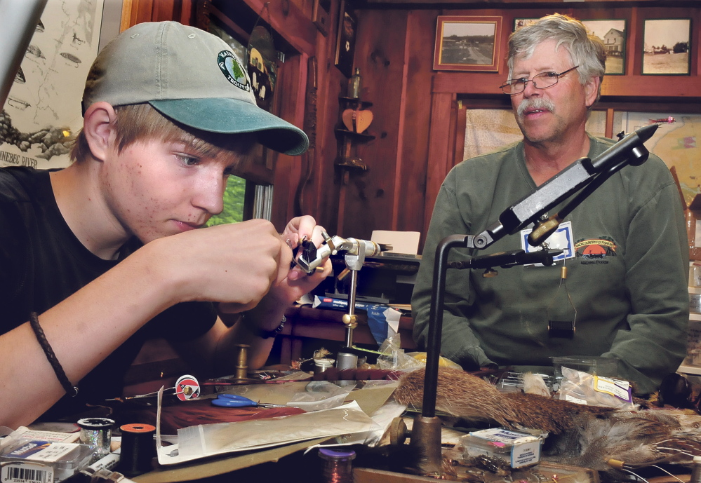 Teenager Sam Kenney works on tying a fly as Jim Dunbar of Winslow watches during a Maine Trout Unlimited Trout Camp in Solon on Thursday.