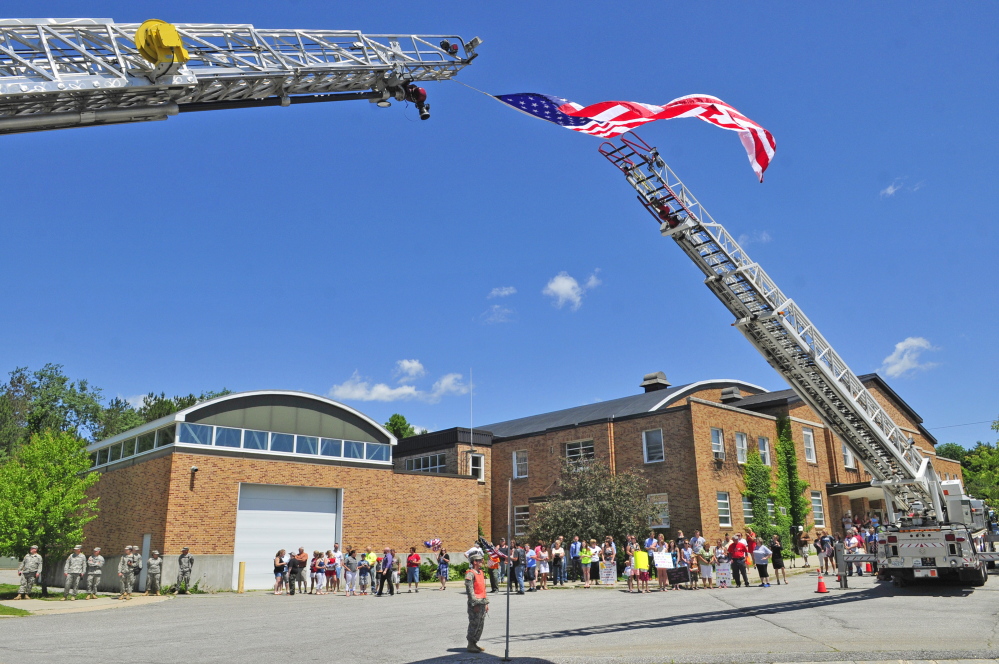 An American flag flies between Winthrop and Augusta fire department ladder trucks as people wait for the bus carrying returning soldiers on Friday at the Augusta Armory.