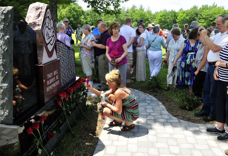 Survivors place roses in front of the Maine Murder Victims’ Memorial Monument at the end of the dedication ceremony on Sunday in Augusta.