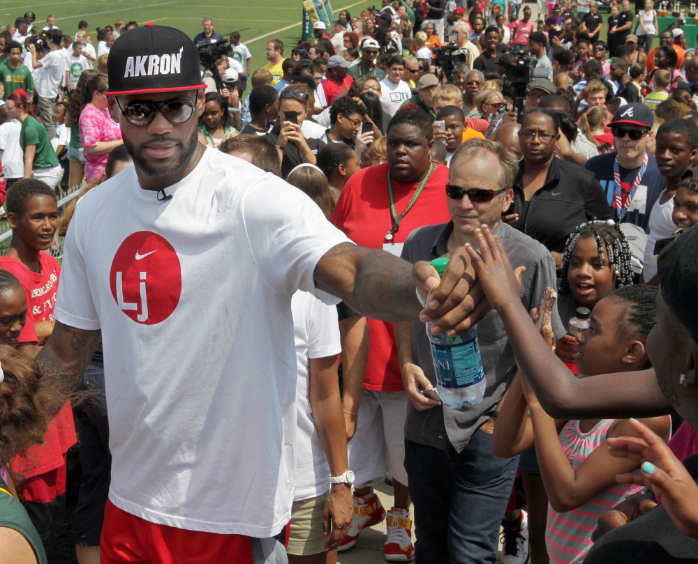 In this Aug. 10, 2013 file photo, Miami Heat’s LeBron James greets a young fan while on the way to an interview at his foundation’s second annual “I Promise Family Reunion,” in Akron, Ohio.