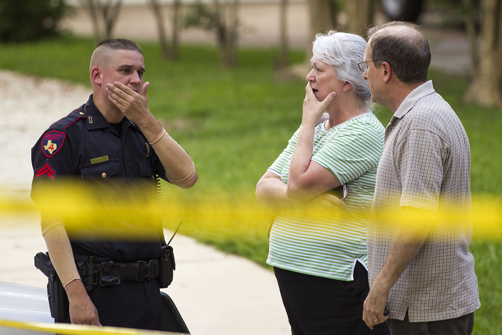 People stand with a law enforcement officer near the scene of a shooting Wednesday in Spring, Texas. A Harris County Sheriff’s Office statement says precinct deputy constables were called to the house about 6 p.m. Wednesday and found two adults and three children dead. Another child later died at a hospital.