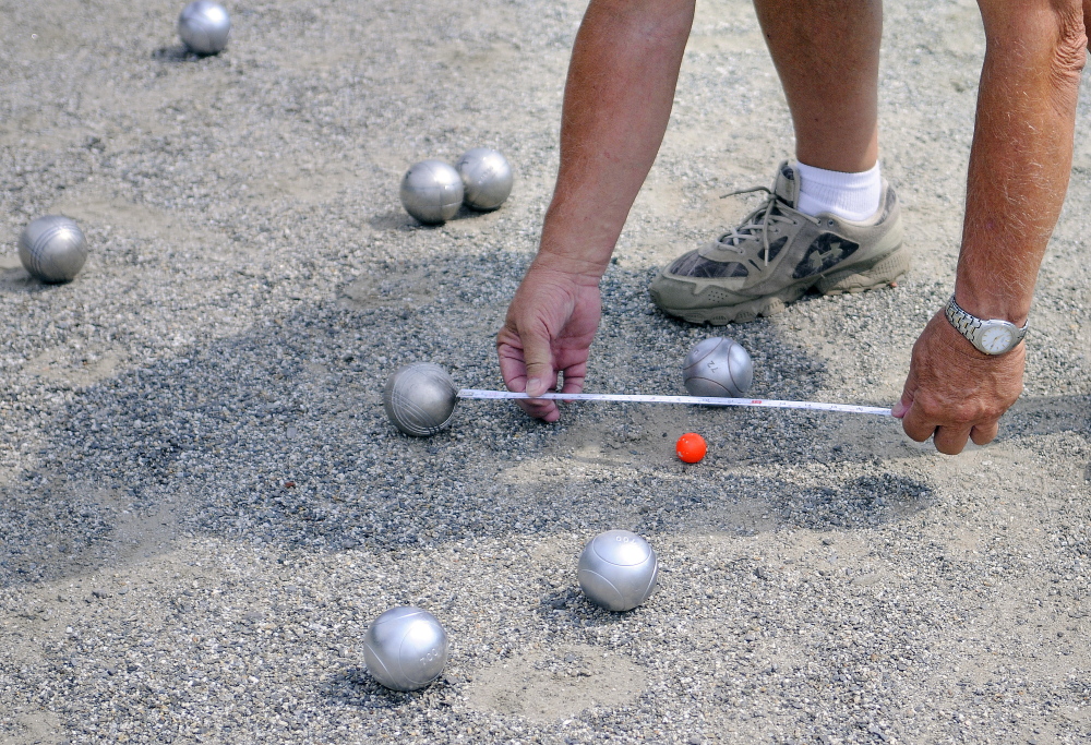 A judge measures the distance Sunday between petanque balls during a tournament at Mill Park in Augusta.