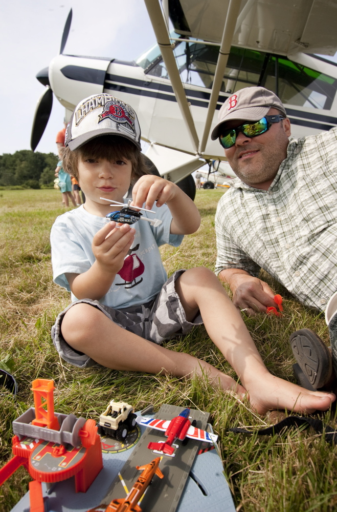 Jed Bucci, 3, of Cape Elizabeth, plays with a toy Sunday while sitting with his father, Jeff Bucci, near the family plane during the fly-in at Sprague Field in Cape Elizabeth.