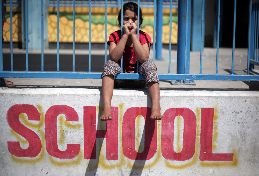 In this Monday photo, a Palestinian girl sits on the wall of the New Gaza United Nations School, where dozens of families have sought refuge after fleeing their home in fear of Israeli airstrikes.