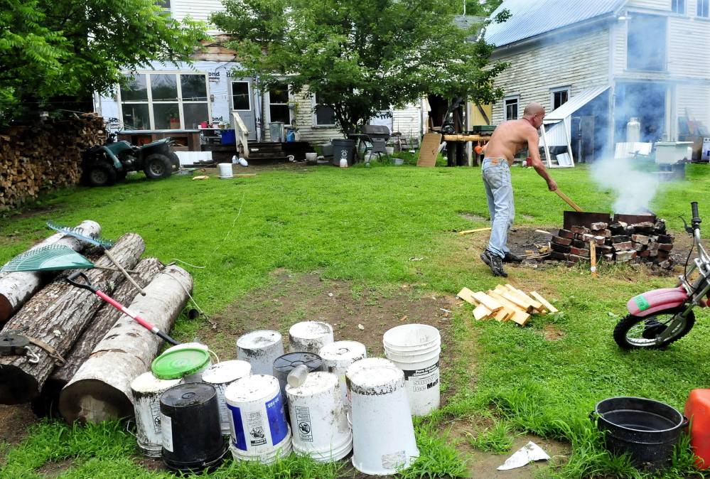 Duane Pollis stokes an outdoor fire pit with wood in the front yard of his home in Wilton on Wednesday. Pollis has removed a considerable amount of items in his yard that put it in violation of a town ordinance. Town officials said this week they are pleased with the progress of the cleanup.