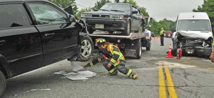 A firefighter puts down pads to absorb fluid leaking from a wrecked car as tow truck drivers clear U.S. Route 202 after a collision at the intersection of Route 202, Bog Road and Blue Road on Wednesday in Monmouth.