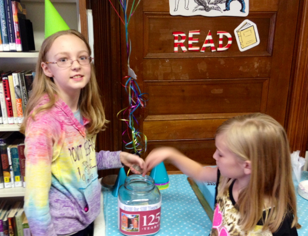 Gracie Demchak, 12, and her sister Maggie, 9, add their money to the Skowhegan Library’s $125 for 125 Years Jar at a party held recently to celebrate the Skowhegan Free Public Library’s 125th birthday. The $125 goal was reached during the party, the money will benefit the library’s renovation.