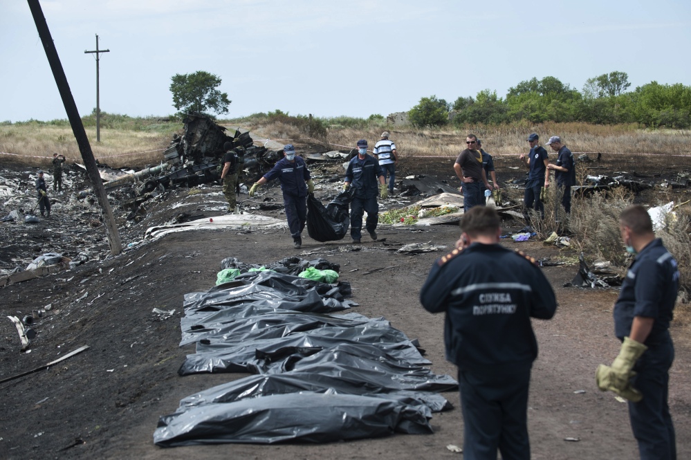 Ukrainian Emergency workers carry a victim’s body in a bag as pro-Russian fighters stand in guard at the crash site of Malaysia Airlines Flight 17 near the village of Hrabove, eastern Ukraine, Sunday.