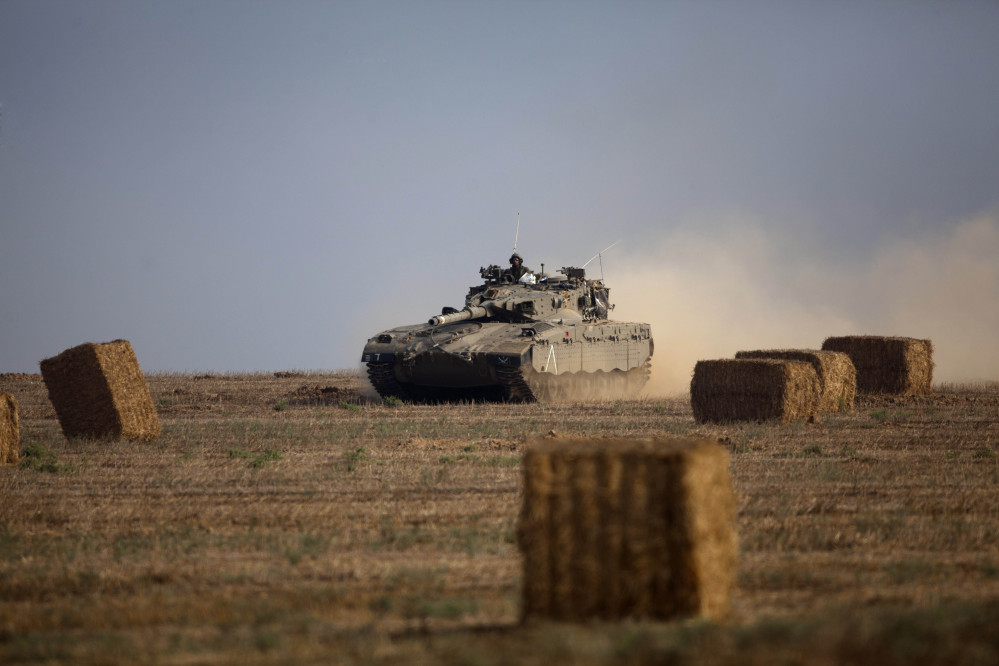An Israeli tank runs between hay bales near the Israel and Gaza border Wednesday. Israeli troops battled Hamas militants near a southern Gaza Strip town, sending Palestinian residents fleeing.