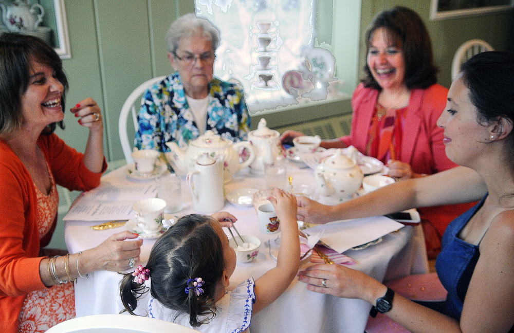 Caroline Merrill, 2, serves herself a sugar cube Monday while having tea with her mother, Jenny Merrill, right, aunts Anita Hopkins, left, and Heather Priest, second from right, and grandmother, May Coffin, top center, at the Blue Willow Tea Room in Randolph.