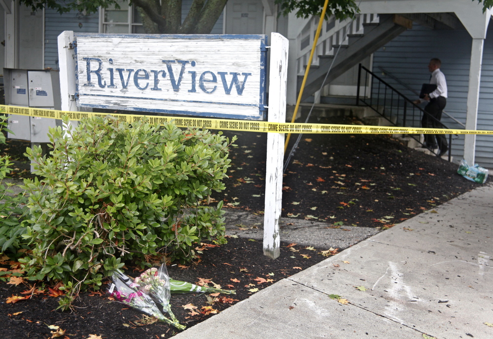 Press Herald photo by Jill Brady
Bouquets of flowers rest at the RiverView apartment building sign as an investigator climbs the stairs to the apartment where five members of one family were found dead at 27 Water St., Saco, on Sunday.