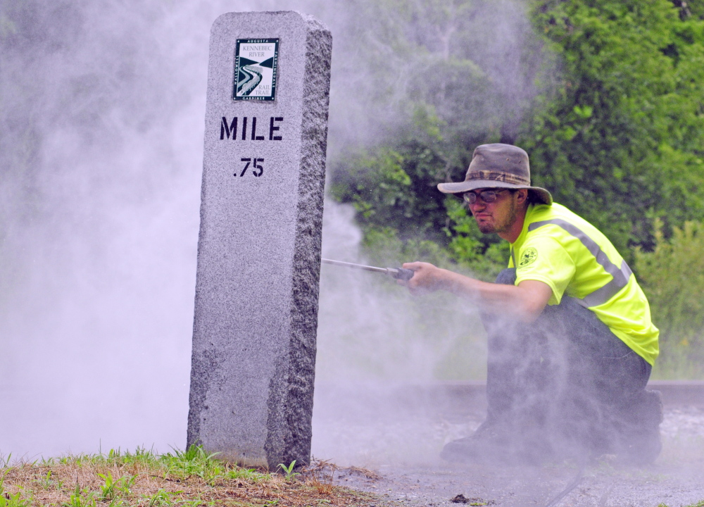 After a city crew scrubbed off graffiti with a solvent, city worker Bryan Hickey rinses a granite Kennebec River Rail Trail milestone on Wednesday in Augusta. City workers and volunteer Kathleen “Sukey” Sikora cleaned off or painted over graffiti that was painted the night before.