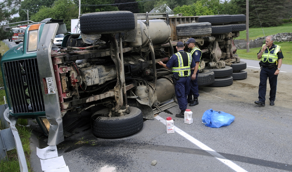 Police inspect an overturned dump truck Tuesday on U.S. Route 202 in Winthrop.  The operator pulled over, according to police, to yield to an ambulance when he lost control.  The driver suffered bumps and bruises, police said, but did not wish to be transported to a hospital. Traffic was reduced to one lane on the road as crews prepared to right the truck.