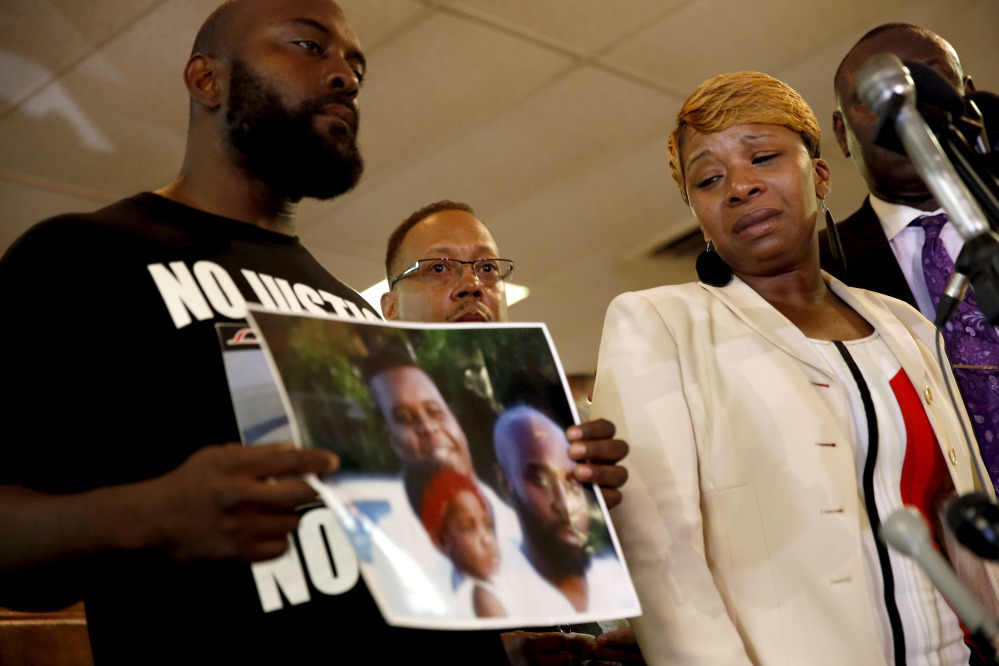 Lesley McSpadden, right, the mother of 18-year-old Michael Brown, watches as Brown’s father, Michael Brown Sr., holds up a family picture of himself, his son, top left in photo, and a young child during a news conference Monday, in Ferguson, Mo.