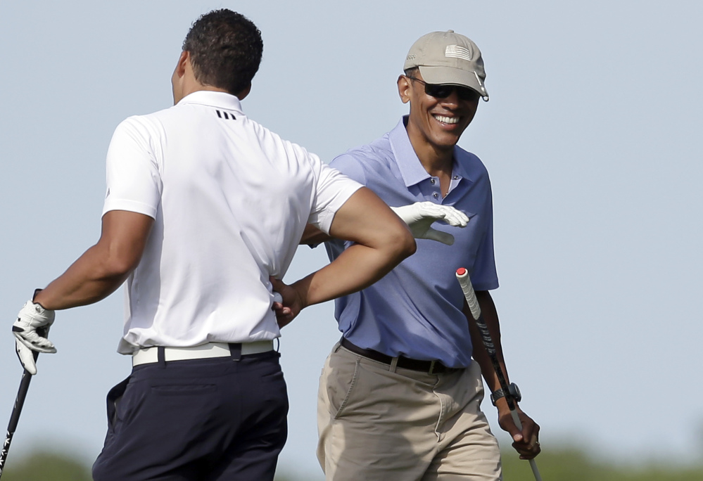 President Barack Obama, right, smiles as he gives a pat on the arm to Cyrus Walker, left, cousin of White House senior adviser Valerie Jarrett, while golfing at Vineyard Golf Club, Tuesday, in Edgartown, Mass., on the island of Martha’s Vineyard.