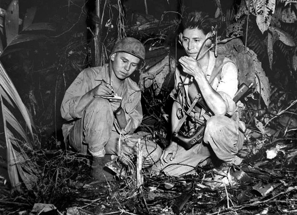 Marine Cpl. Henry Bake Jr. and Marine Pfc. George H. Kirk, Navajo Indians serving with a Marine signal unit, operate a portable radio set in a clearing they’ve hacked in the dense jungle close behind the front lines in December 1943 at Bougainville, in the territory of New Guinea.