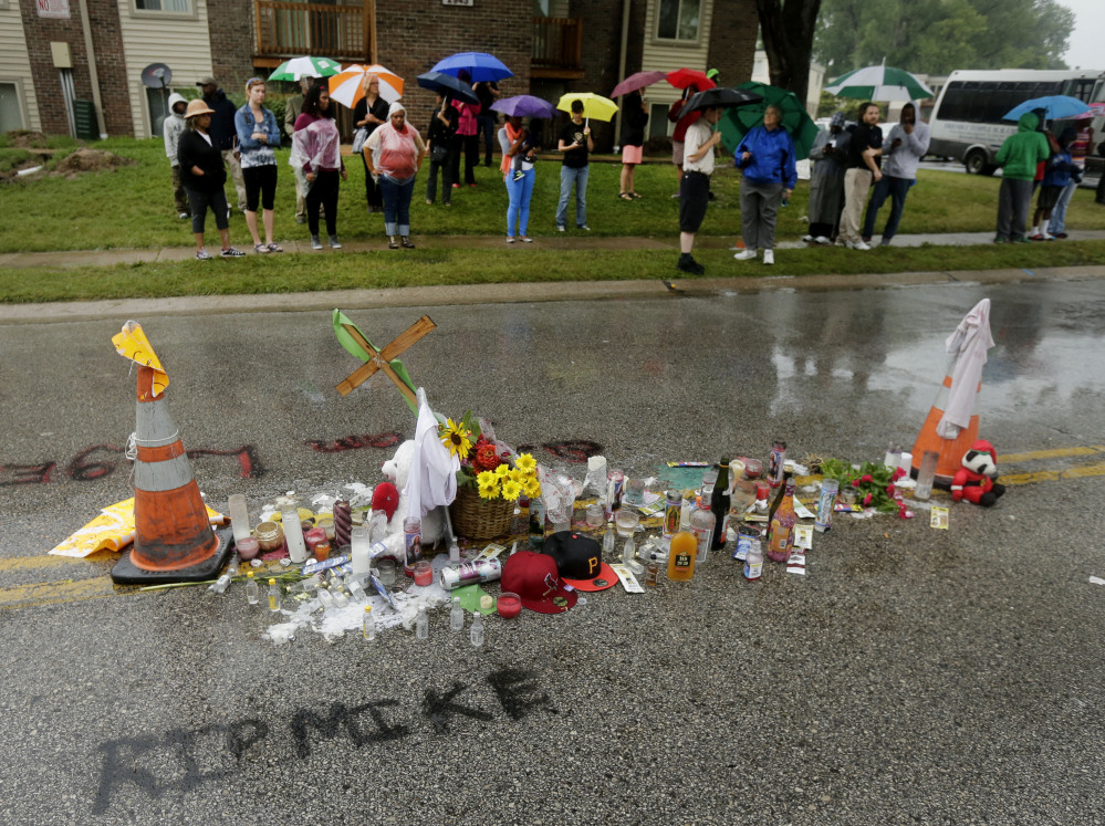 People gather next to a makeshift memorial for Michael Brown on Saturday, located at the site where Brown was shot by police a week ago in Ferguson, Mo. Brown’s shooting in the middle of a street following a suspected robbery of a box of cigars from a nearby market has sparked a week of protests, riots and looting in the St. Louis suburb.
