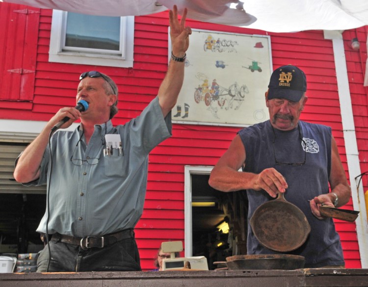 Auctioneer Brian Huntley, left, sells the collection of cast iron pans that Mike King is showing the crowd during the Coopers Mills Volunteer Fire Department charity auction on Saturday.