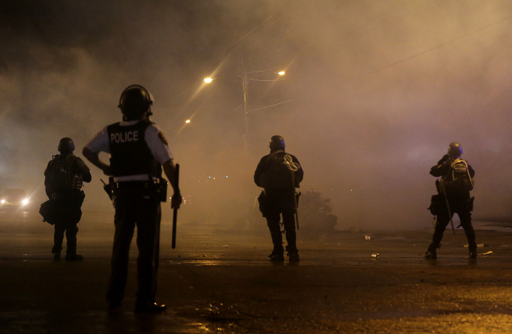 A law enforcement officer watches early Sunday as tear gas is fired to disperse a crowd protesting the shooting of teenager Michael Brown last Saturday in Ferguson, Mo.