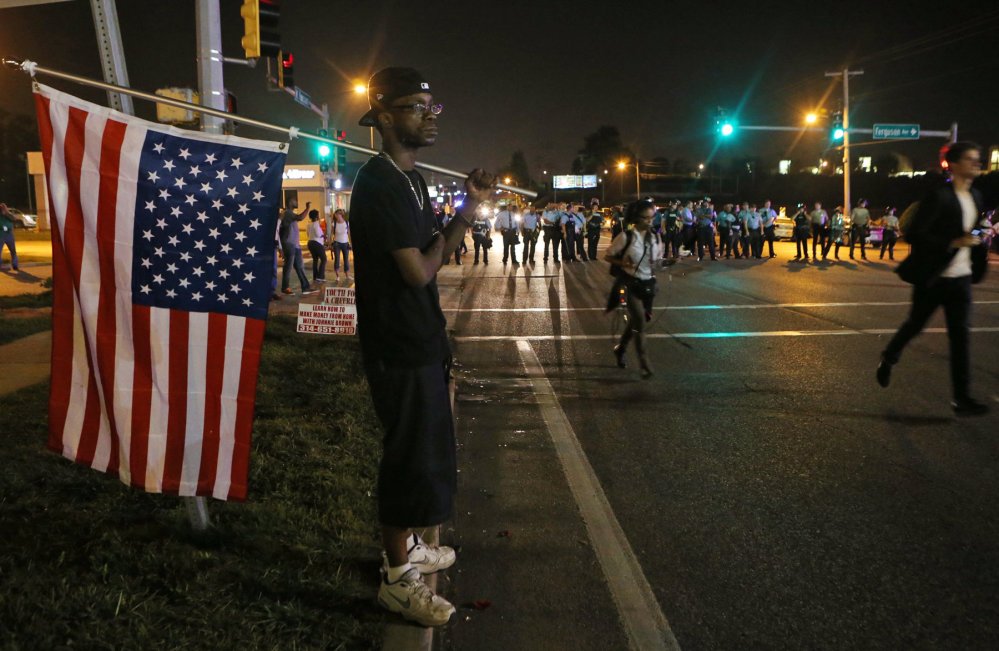 A protester watches the confrontation between the police and demonstrators Monday in Ferguson, Mo.