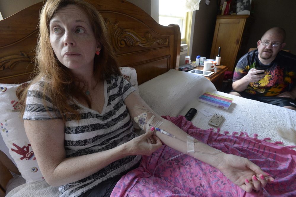 Lisa Lawlor of Saco adjusts her IV as she takes antibiotics, part of her routine to manage her many Lyme disease-related symptoms. Her friend Lee Faulkner of Saco is at her bedside. She noticed a rash in 2011, but was not diagnosed until 2013.