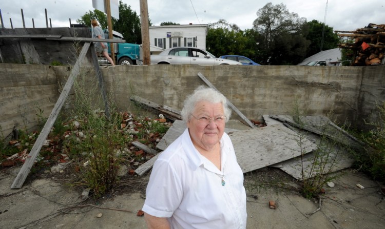 Alice Emery stands in the foundations of two burned out buildings on Main Street in Norridgewock on Friday. Emery was housekeeper for Harold Alfond for 45 years and has taken on the mission to turn the eyesores into green space for the community.