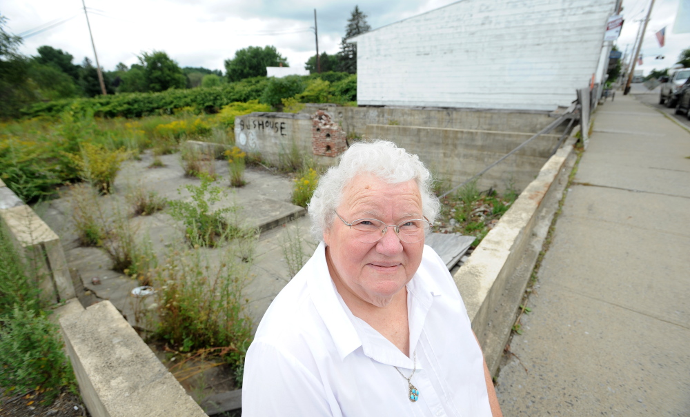 Alice Emery stands in the foundations of two burned out buildings she has bought and donated to the town of Norridgewock for development on Friday.