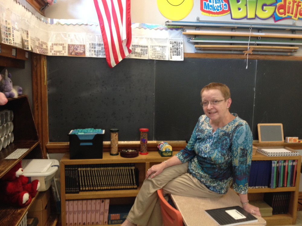 Laura Bushey sits below class photos from her first years of teaching. Bushey, who says the first day of school is her favorite day of the year, lines her classroom with class photos from her 39 years teaching.
