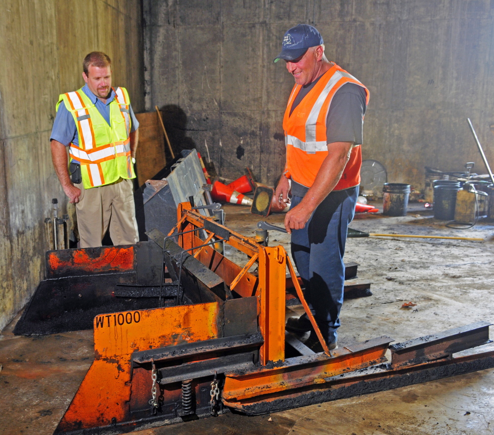 Augusta Public Works employees Jerry Dostie, left, and Mike Morrison talk about the WT1,000 during an interview Wednesday in Augusta. Morrison invented the machine, which is pushed by a skid steer and levels paving being put into the wheel tracks on a road.