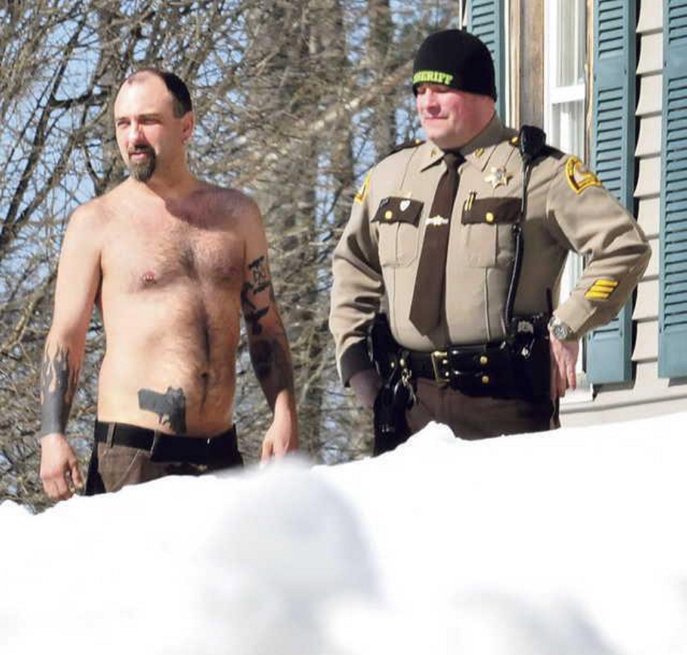 Norridgewock resident Michael Smith stands beside a Somerset County Sheriff deputy after he was coaxed out of his home by police on March 18. The tattoo of a pistol on his stomach was mistaken for a real firearm earlier, resulting in a call to police. No charges were filed.