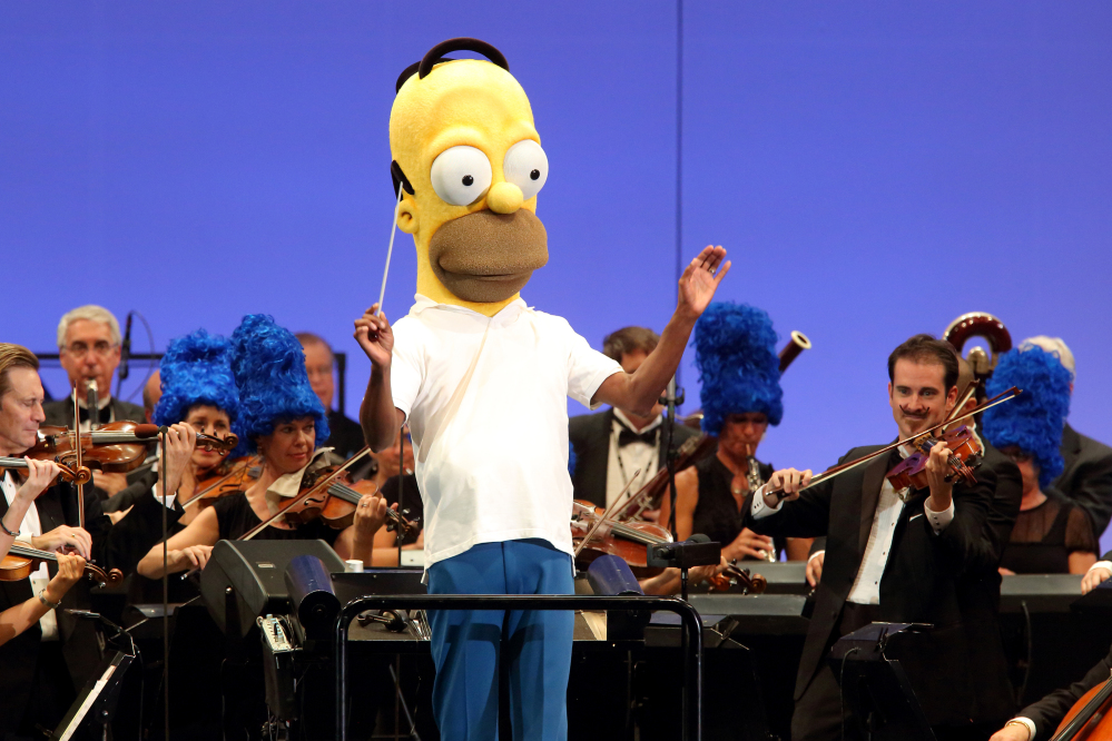 In this photo provided by the Hollywood Bowl, the orchestra, led by conductor Thomas Wilkins in a Homer Simpson costume, performs at the world premiere of “The Simpsons Take the Bowl” at the legendary concert venue Friday in Los Angeles.