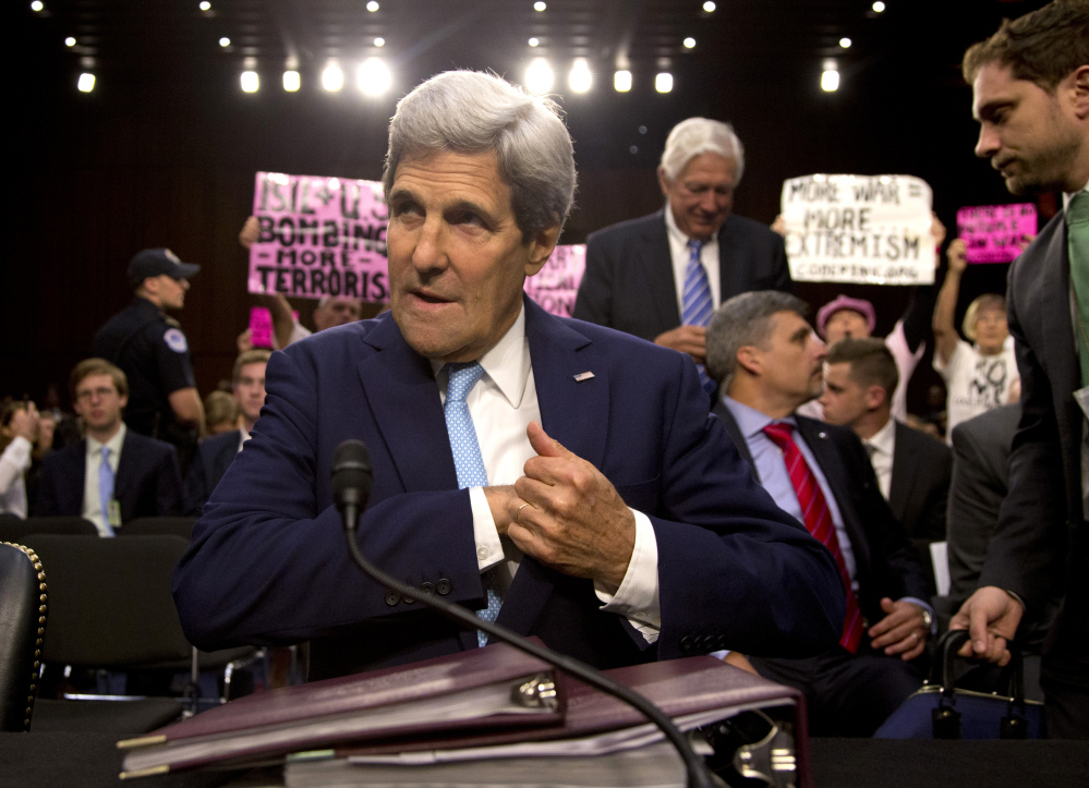As protesters from CodePink hold up signs and shout behind him, Secretary of State John Kerry settles into his seat as he arrives to testify on Capitol Hill in Washington on Wednesday during a Senate Foreign Relations Committee hearing on the U.S. strategy to defeat the Islamic State group.