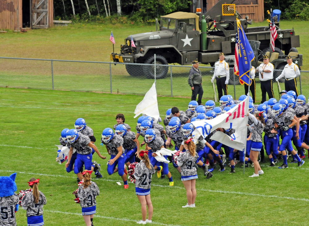 Members of the Oak Hill football team take the field in their camouflage uniforms before a game Saturday against Dirigo.