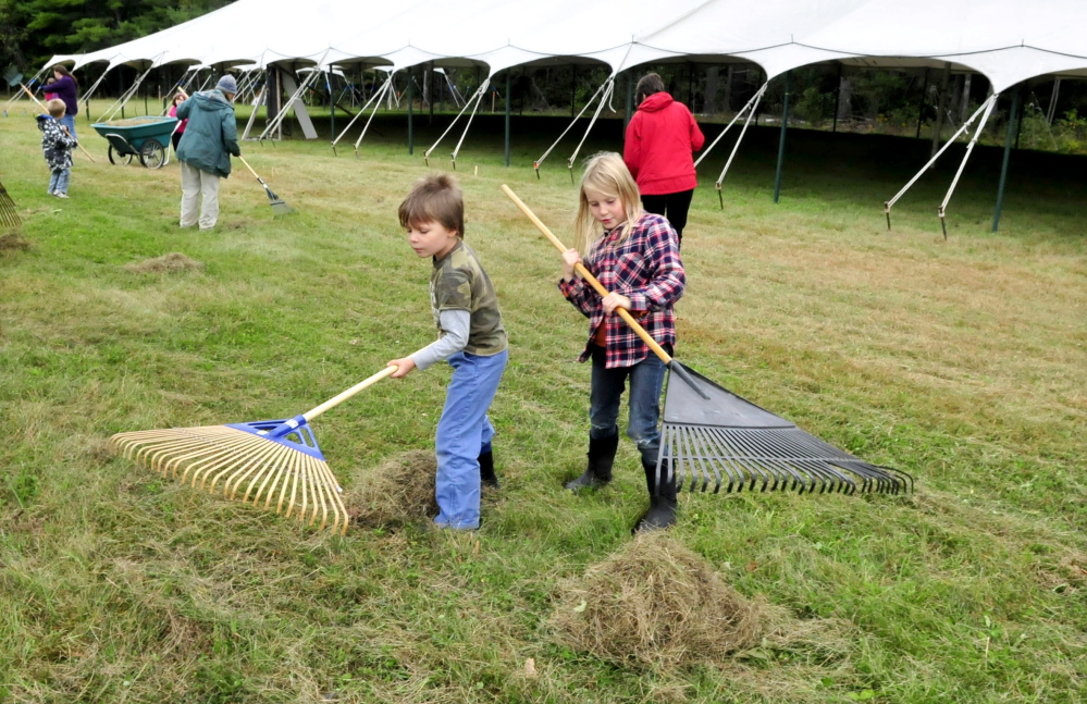 Volunteers Forest Pitkin and Juniper Fowler on Tuesday help rake mowed grass outside a vendor tent while preparing for the three-day Common Ground Country Fair that begins this Friday in Unity.