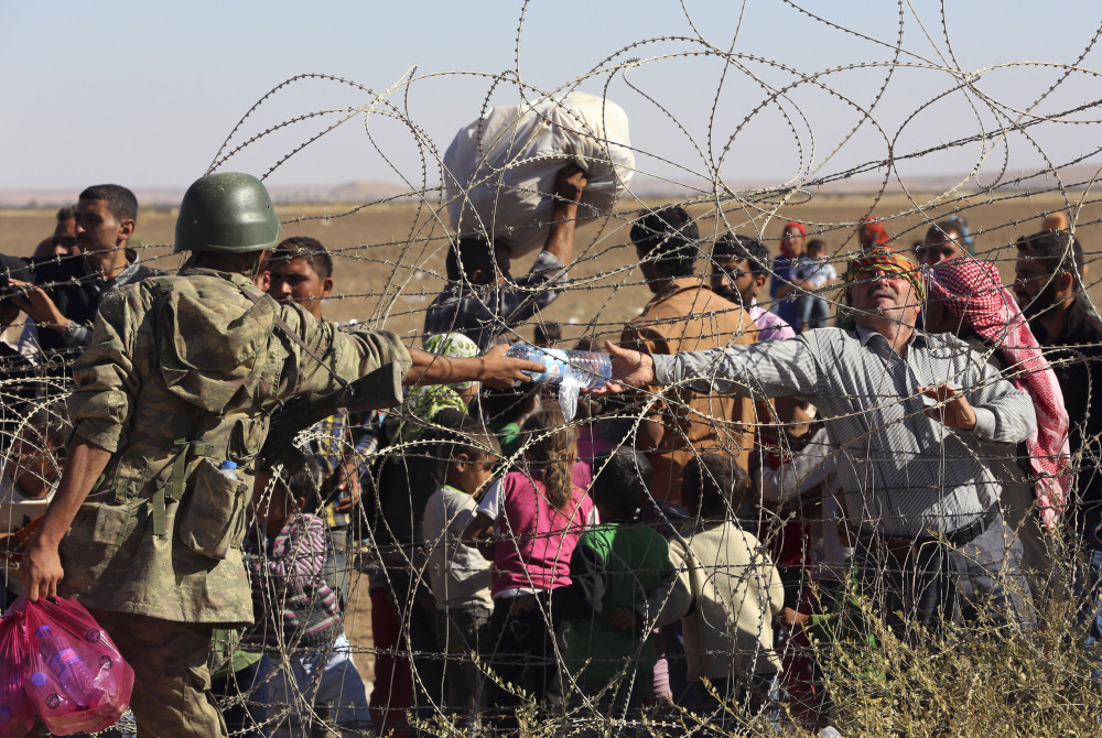 A Turkish soldier gives a bottle of water to a handicapped Syrian refugee waiting at the border in Suruc, Turkey, Sunday. Turkey opened its border Saturday to allow in up to 60,000 people who massed on the Turkey-Syria border, fleeing the Islamic militants’ advance on Kobani.