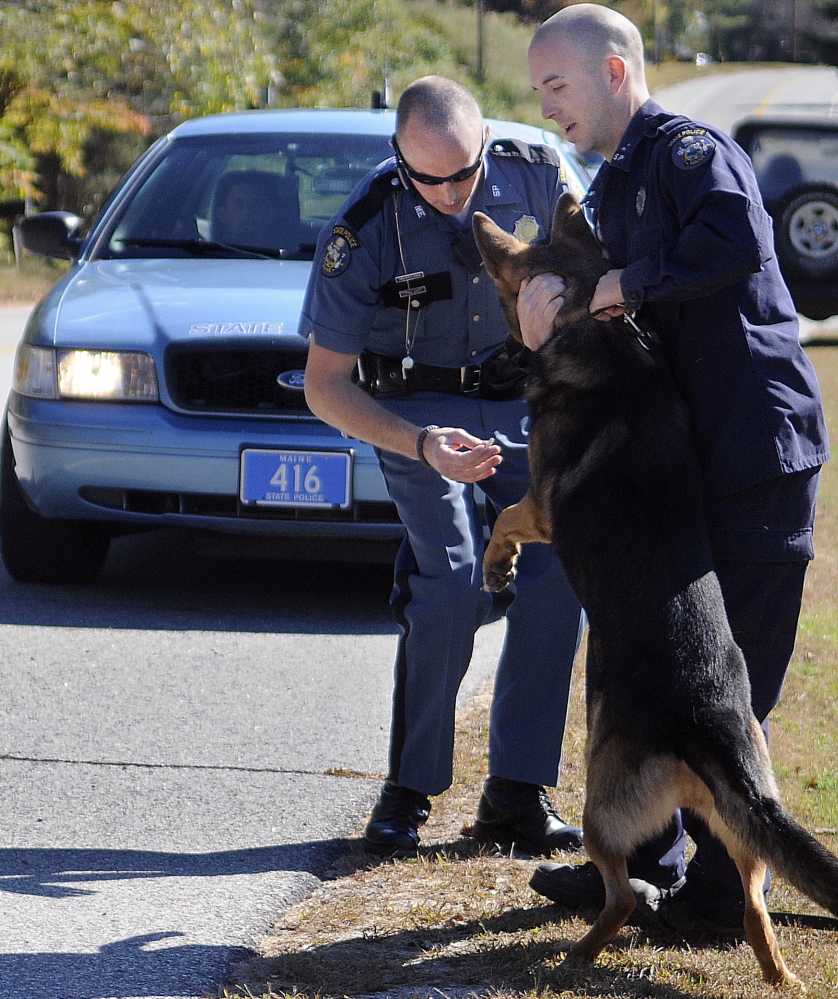 Maine State Trooper Eric Verhille, right, restrains his dog Monday as Trooper Chris Rogers collects evidence following the arrest of Scott Howard in South Gardiner. Howard was charged with a number of counts after allegedly threatening to burn down his former girlfriend’s home and kill her dog.
