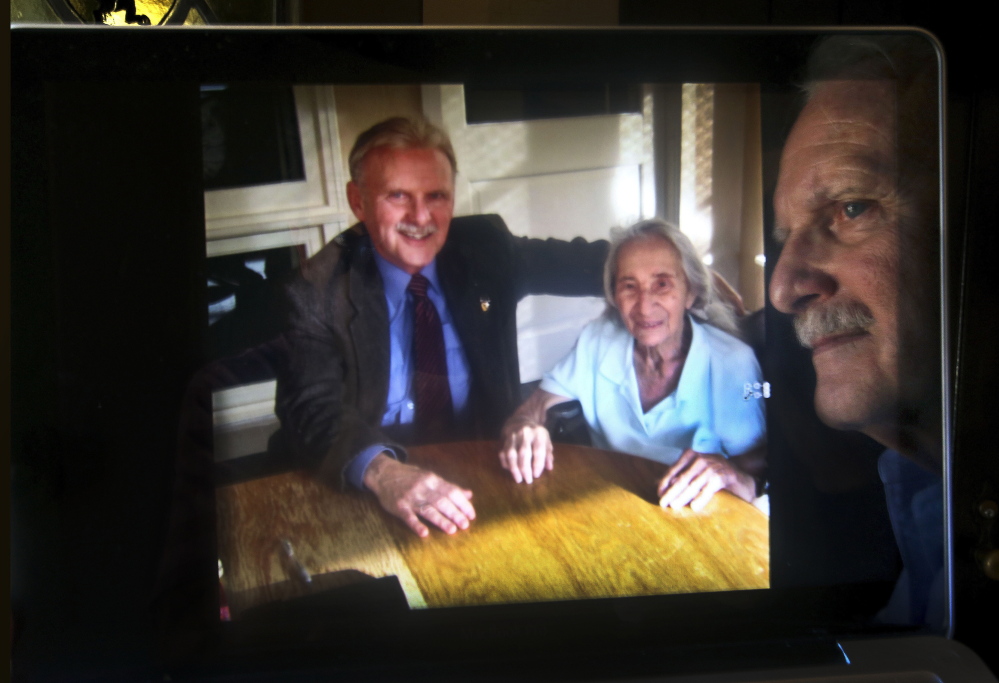James Caccavo is reflected in his computer screen, next to a photograph of him with his elderly neighbor Sarah Cheiker, taken at a health care center in Fryeburg, Maine, back in 2012, where she is currently living. Cheiker, now 88, disappeared in 2008 from her home in Los Angeles that was later bulldozed and replaced by a bigger house.