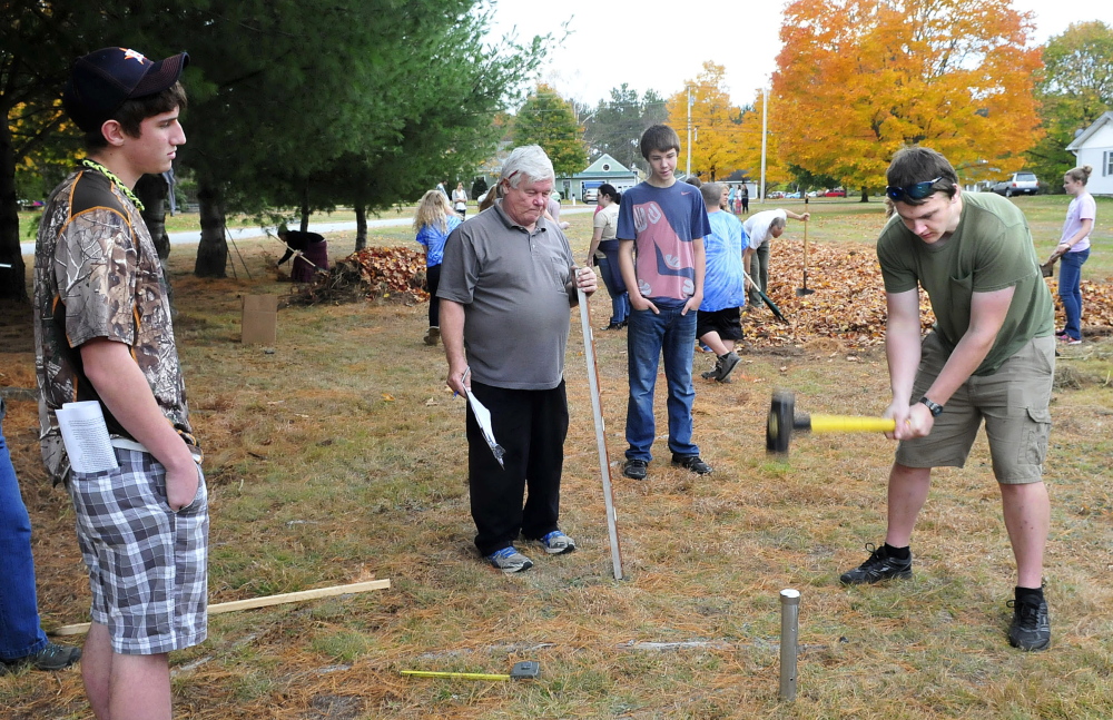 Carrabec High school student Eli Pease pounds in a boundary stake as student Christian Miller, left, Technical Trades instructor Fran Sirois and Darren Hassell watch at the North Anson school on Wednesday.