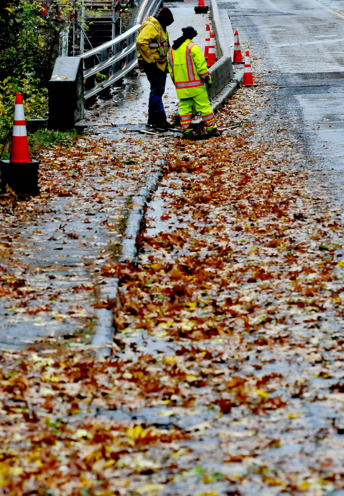 Waterville Sewage District employees Jason Webster, left, and Lance Gagnon unclog a drain in Waterville during a steady rain on Thursday. Gagnon said crews have been busy this week with the wind and rain.