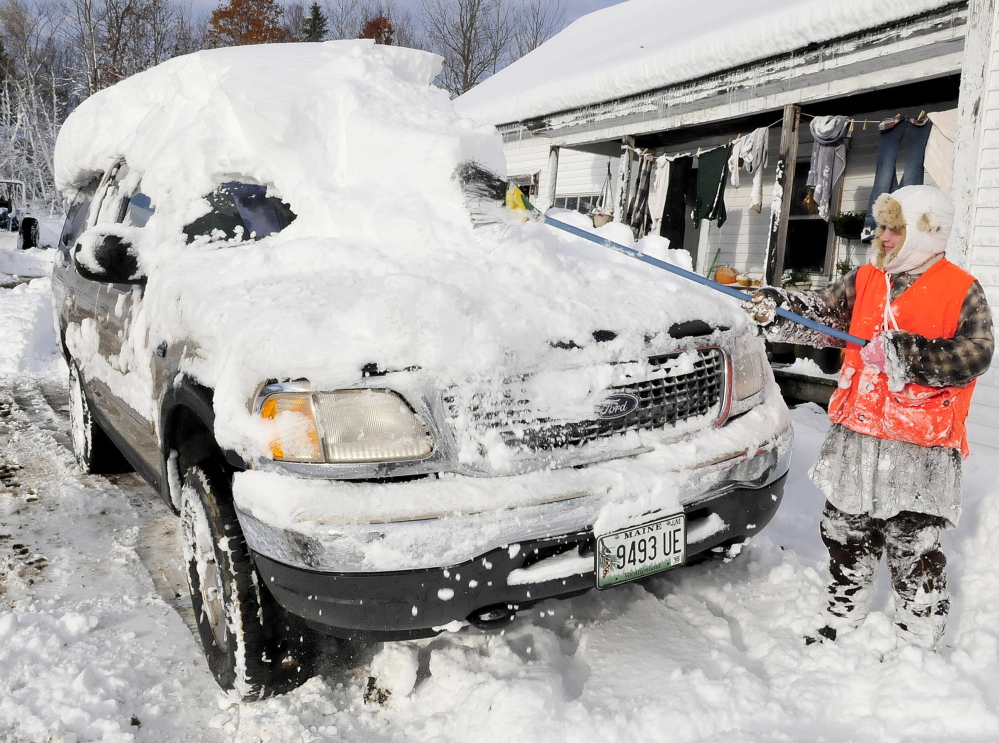 Sydney Astbury uses a broom on Monday to clear the nearly foot of snow that buried the family vehicle at her home in Troy. Many area towns near Troy are without power as wind and heavy snow hit the area on Sunday.