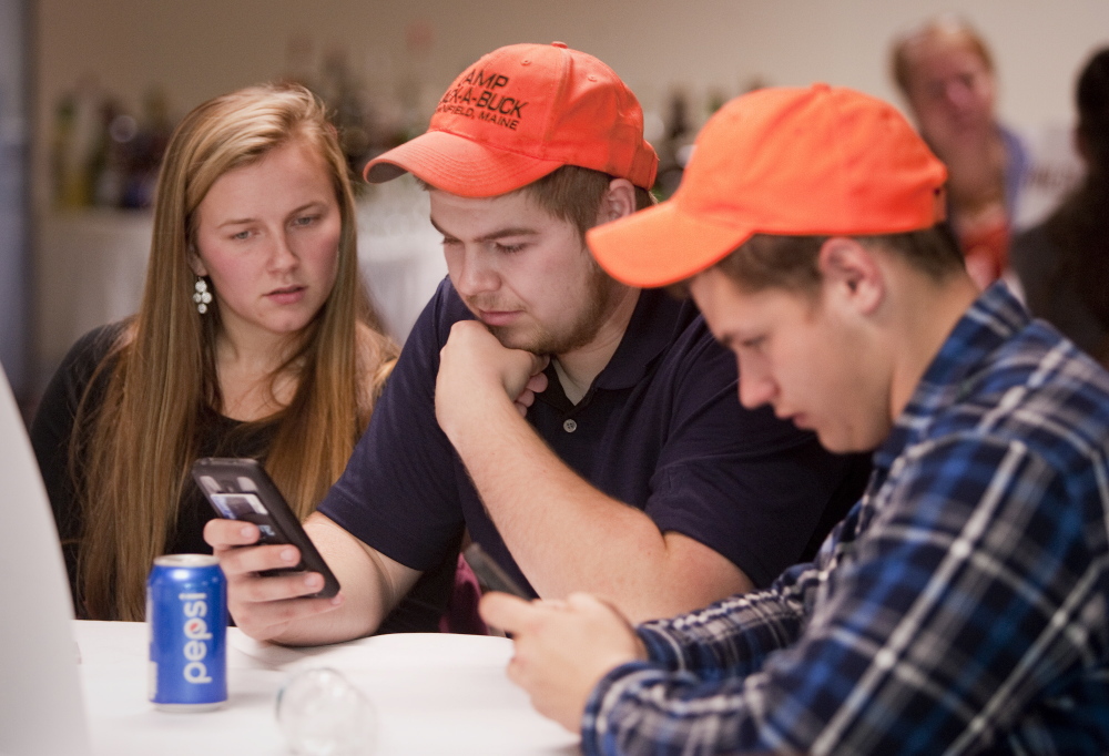 No On 1 bear referendum supporters Brianna Pelkie, of Fryeburg, Walker Day, of Lovell, and Caleb Winslow, of Parsonsfield, check the returns on their phones during an election night gathering Tuesday at the Black Bear Inn in Orono.