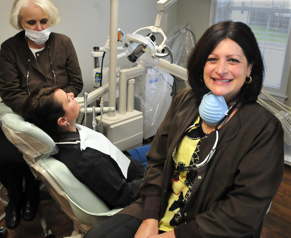 Demi Kouzounas, right, a dentist and co-founder of Dentists Who Care for ME, will offer free dental care Friday to people without insurance at Northwoods Dental in Skowhegan. At left, technician Jayne Hart prepares Denise Bateman for an exam.